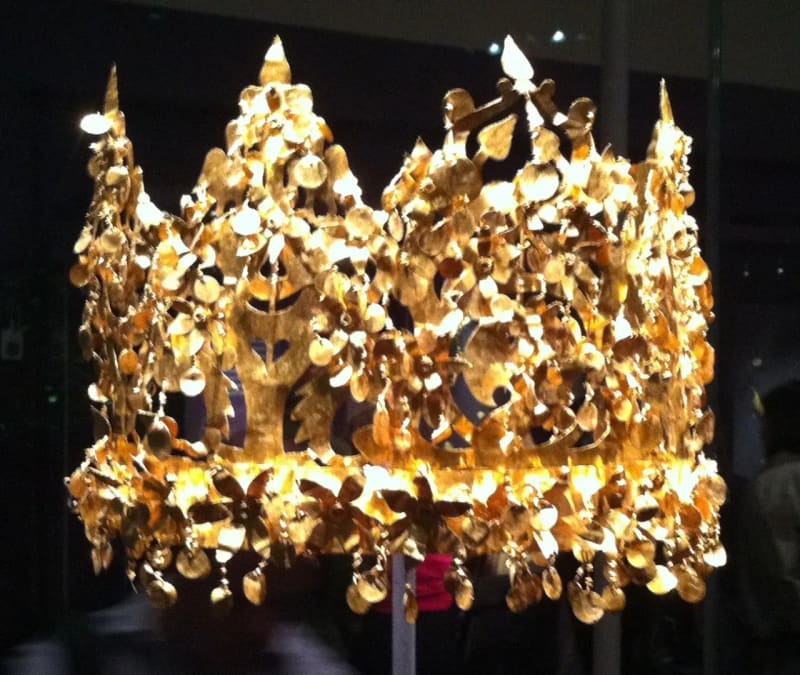 A gold crown of thin hammered leaves, flowers and birds against a dark background.